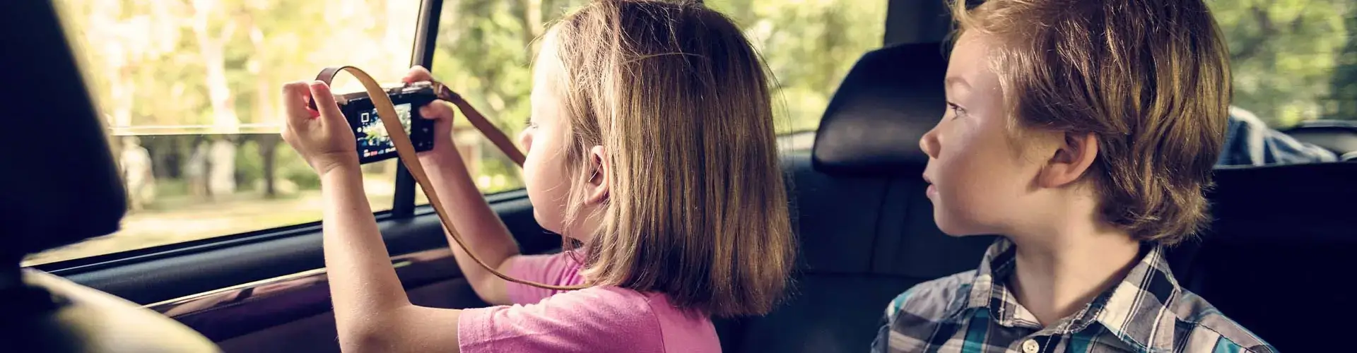 Jong meisje trekt vanuit auto een foto van buiten terwijl jongen naast haar zit