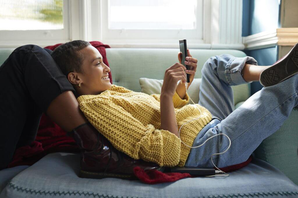 Vrouw ligt in zetel terwijl ze naar haar smartphone kijkt